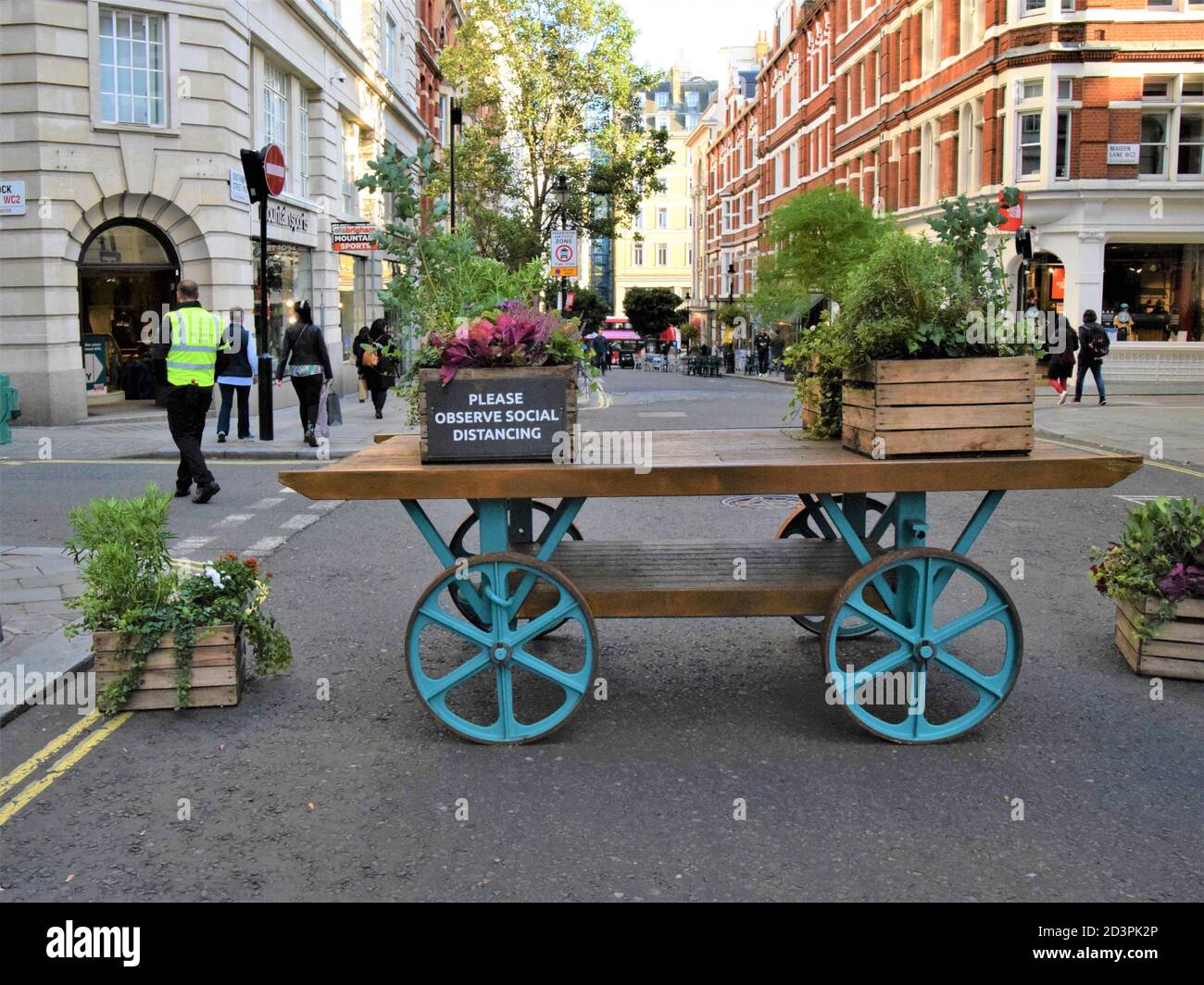 Please Observe Social Distancing street sign and traffic restriction barrier in Covent Garden, London, 2020. Signs and similar carts have been placed around Covent Garden to restrict vehicle traffic and facilitate social distancing during the pandemic. Stock Photo