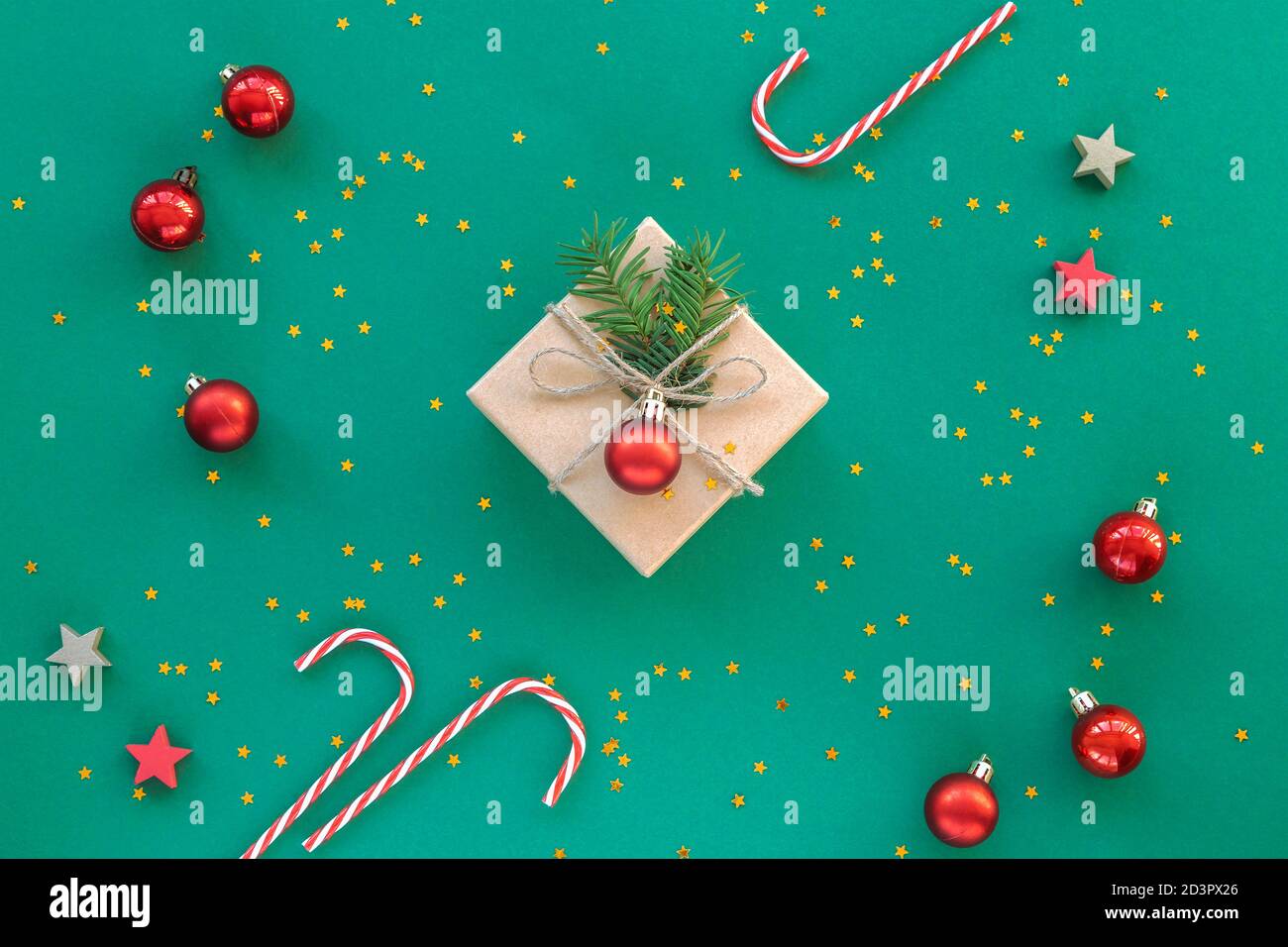 Christmas gift in a box with confetti and red baubles on green background. New year concept. Top view, flat lay, copy space. Stock Photo