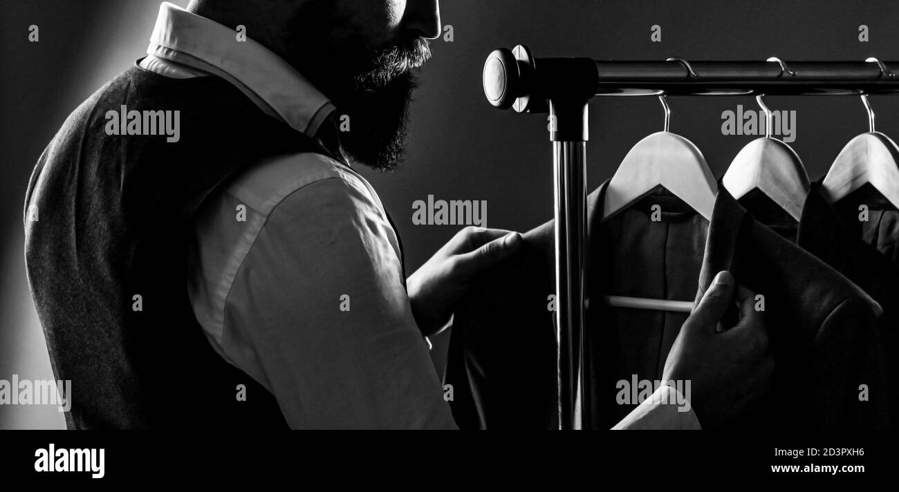 Stylish men's suit. Man suit, tailor in his workshop. Male suits hanging in a row. Men clothing, boutiques. Tailor, tailoring. Black and white Stock Photo