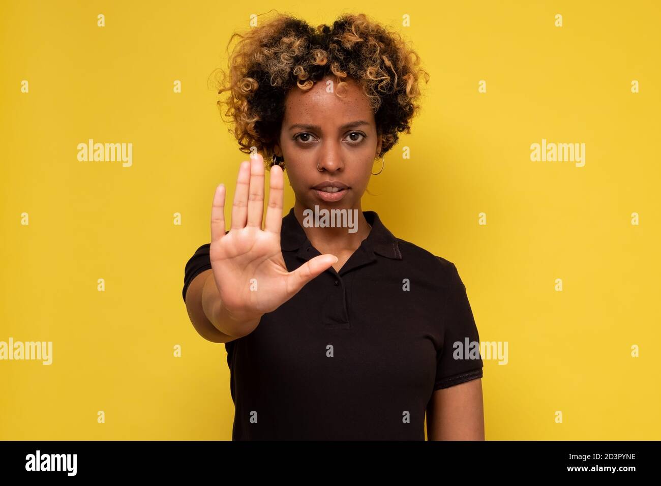 Young woman makes a gesture stop, on a yellow background Stock Photo
