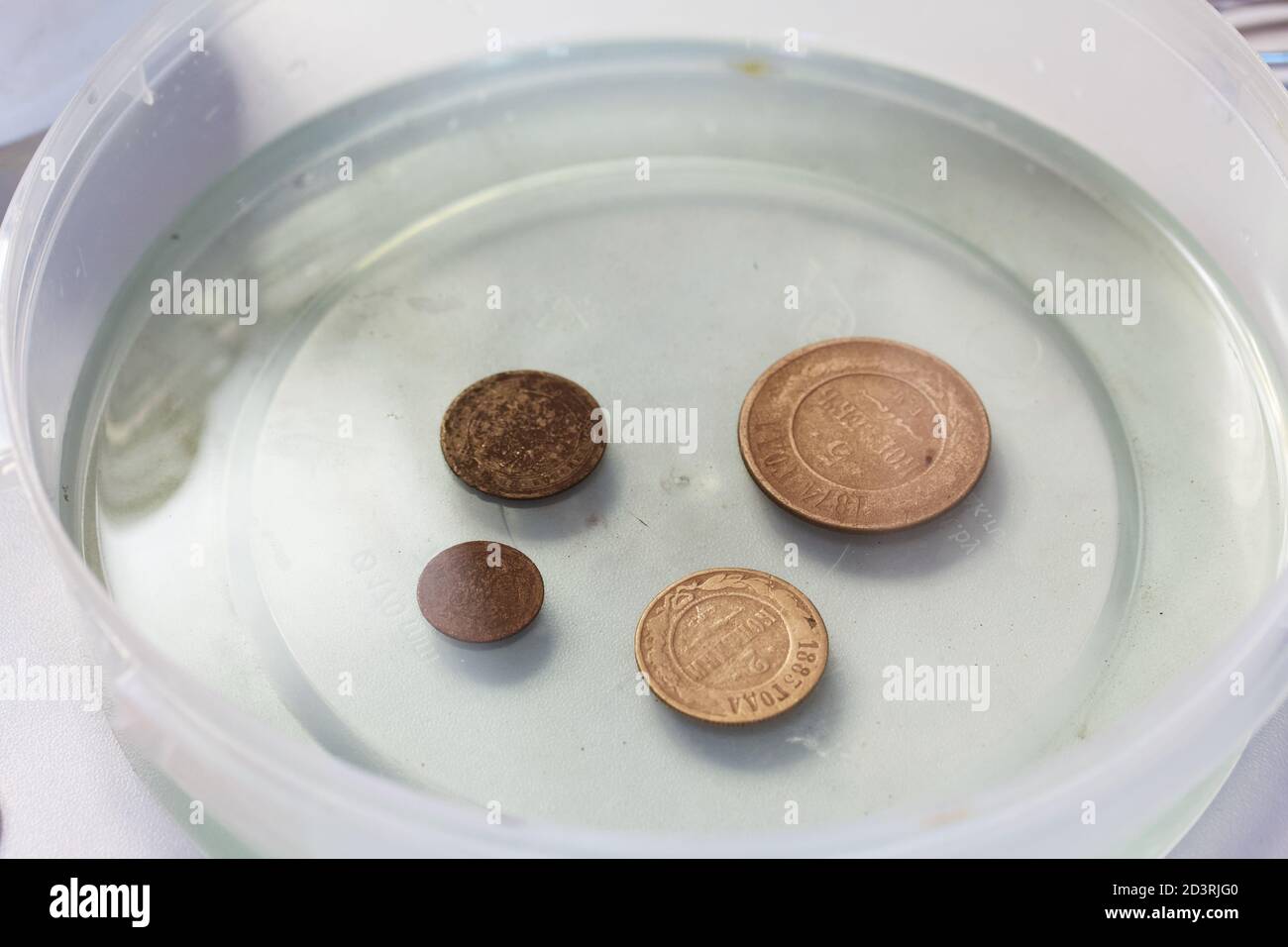 Corroded copper coins. They lie in a container with phosphoric acid.  Prepare for their cleaning and patina Stock Photo - Alamy