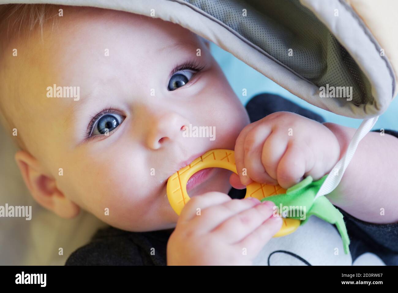 Cute blueeyed baby chewing on a teether covered by a blanket Stock