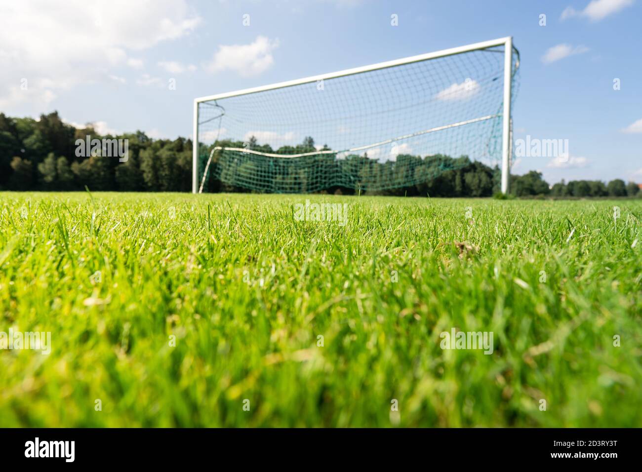Focus on green grass of a football field with blurry goal in the background. Stock Photo