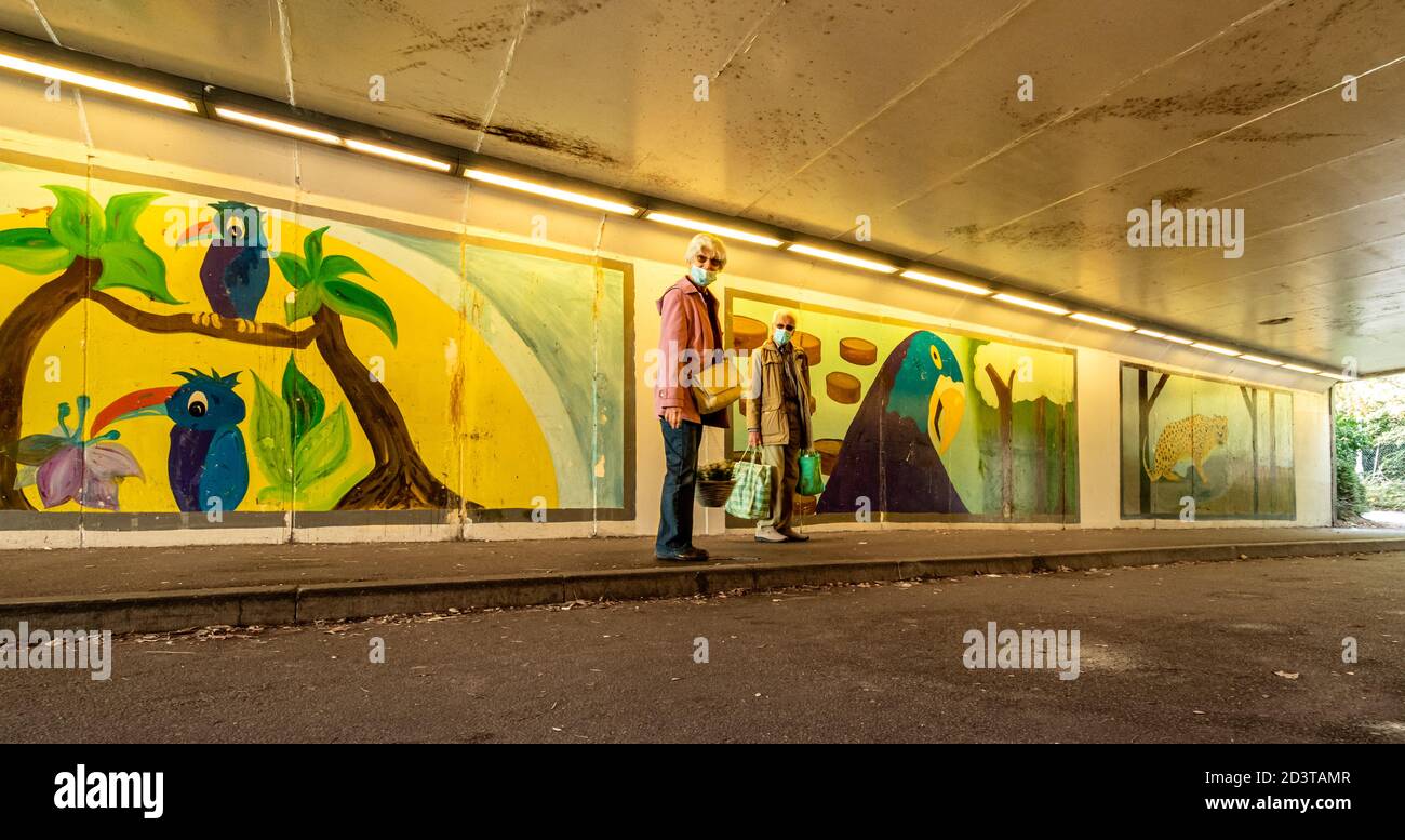 Colourful wall paintings or street art in a subway or underpass in Aldershot town, Hampshire, UK with a senior couple wearing face masks Stock Photo