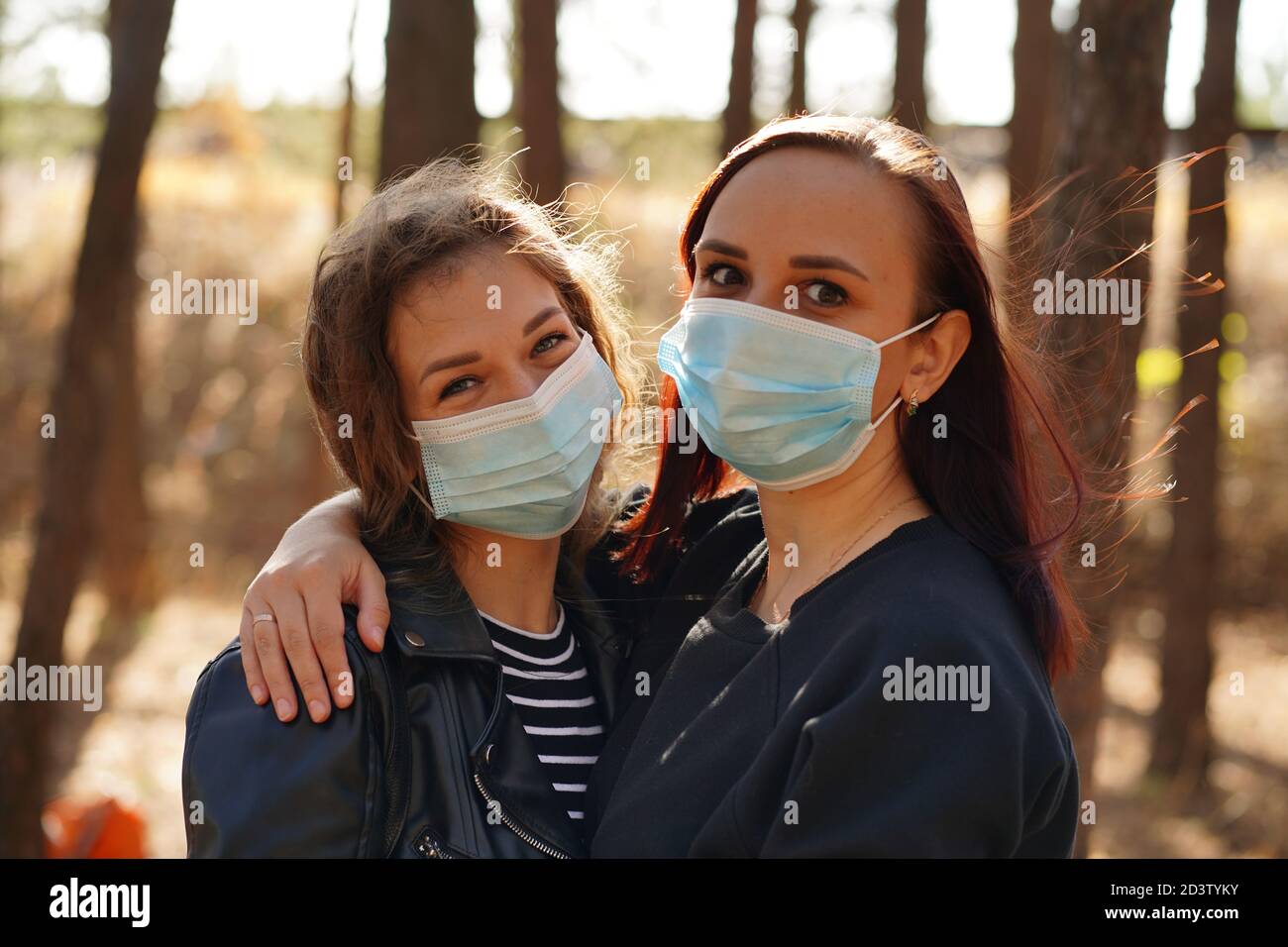 Two young women in medical masks look at camera in wood. Close up of ...