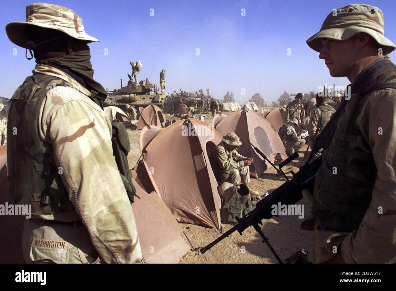US Marine Lance Cpl Eric from San Antonio, Texas holds a SAW, a Squad Automatic Weapon, which holds 200 rounds of 5.56 machine gun bullets, standing with a friend with his face covered in a cloth near a line of tents outside the US Marines operating base in southern Afghanistan December 3, 2001 during a sand storm. Behind are LAV (Light Armoured Vehicles) used for patrols and forward reconnaissance missions. The US Marines PAO (Press Affairs Office) has asked journalists in southern Afghanistan not to use last names as there has been security concerns with family members in the United States.  Stock Photo