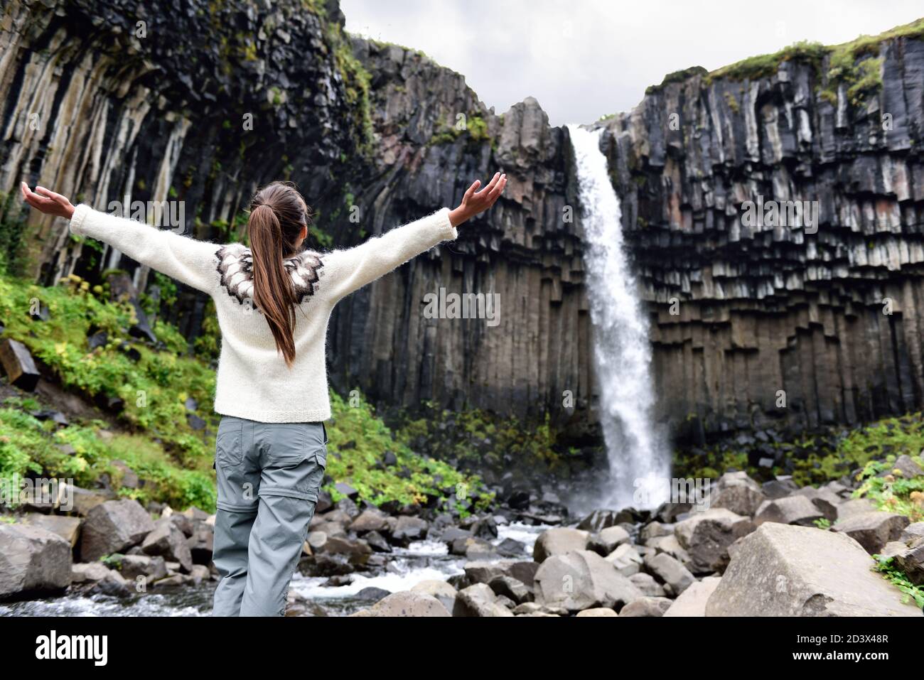 Iceland. Woman enjoying majestic Svartifoss waterfall. Female is visiting famous tourist attraction of Iceland. Spectacular natural landmark on Stock Photo