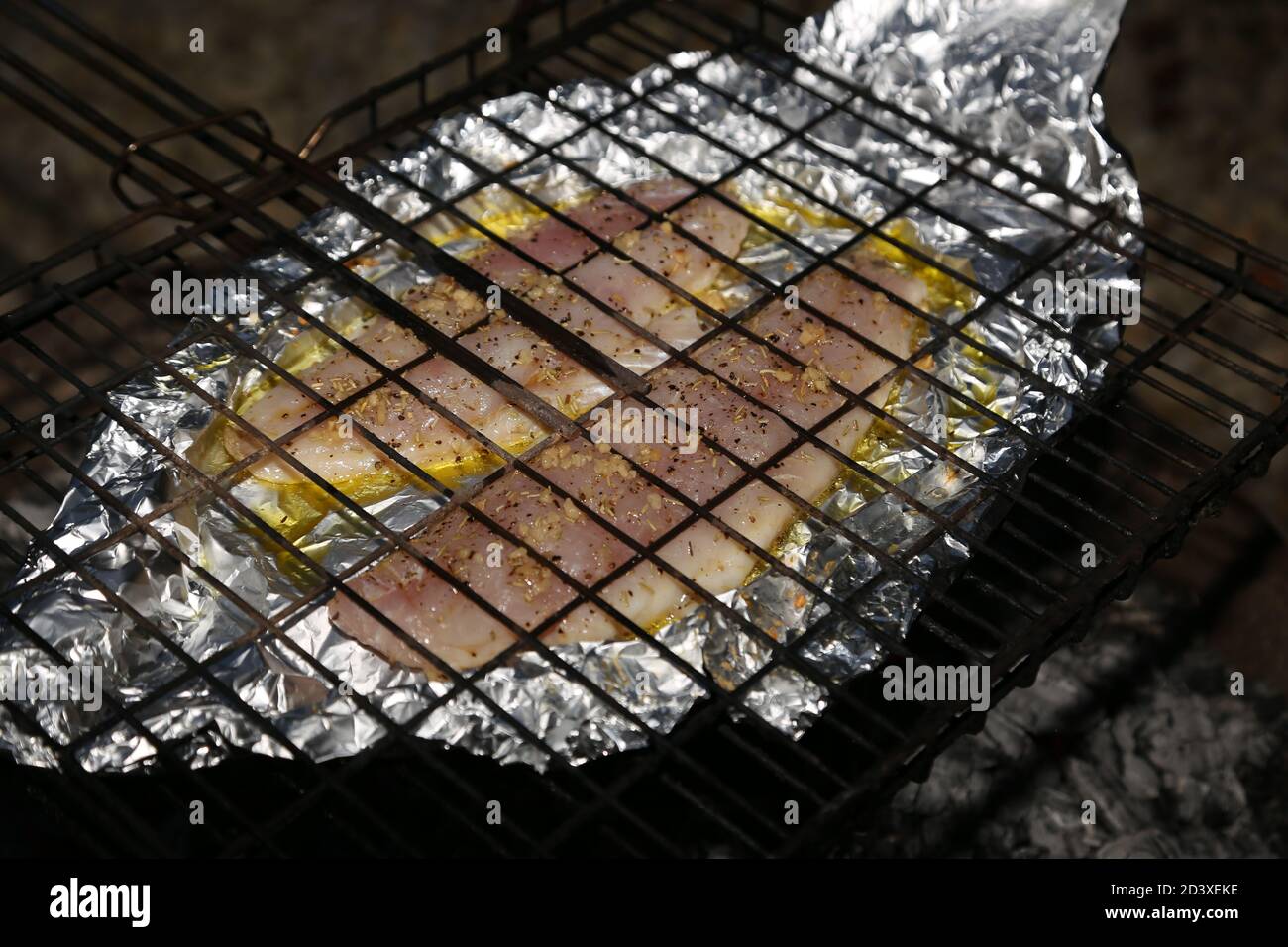 Fish fillets in foil being cooked using a braai grid and hot coals