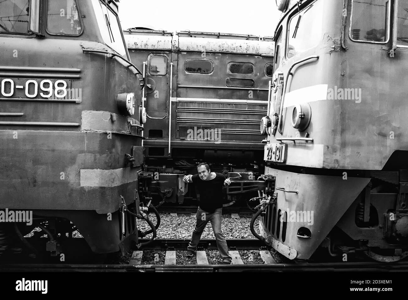A man clamped in a Vice between two cars. Black-and-white photo of a man constrained by circumstances. The guy on the tracks is trapped by machinery. Stock Photo