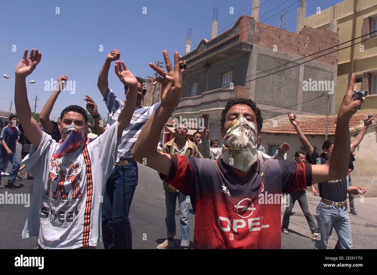 Youths with masked faces in Algeria's Berber-speaking Kabylie region raise their arms as they chant during clashes with gendarmes in El Esnam, 130 kms east of Algiers, May 29, 2001. Berber protesters demand the complete withdrawal of the 10,000-strong gendarme force whom they accuse of brutality and corruption. Riots, fanned by social and economic frustrations, broke out in the region on April 18 after a teenager died in the custody of the gendarmerie, an elite paramilitary force. Stock Photo