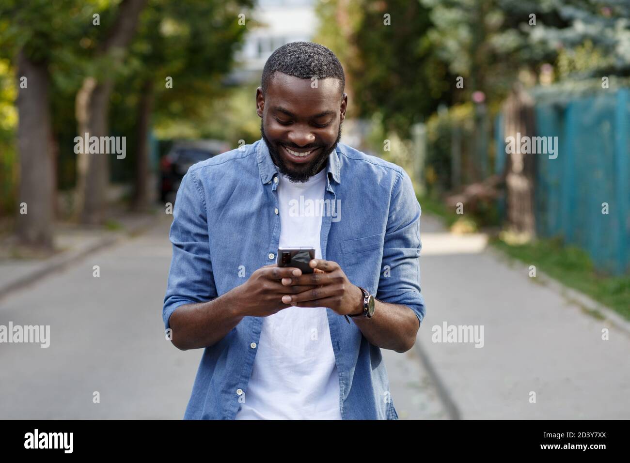 Happy man using mobile phone apps, texting message, browsing internet, looking at smartphone. Handsome Afro-American man using smartphone and smiling Stock Photo