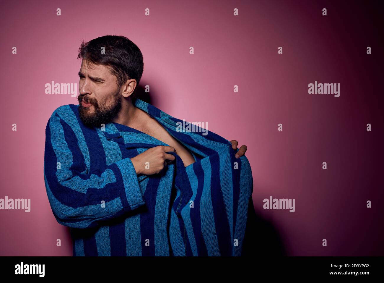 Bearded man in a blue striped robe on a pink background with hands ...