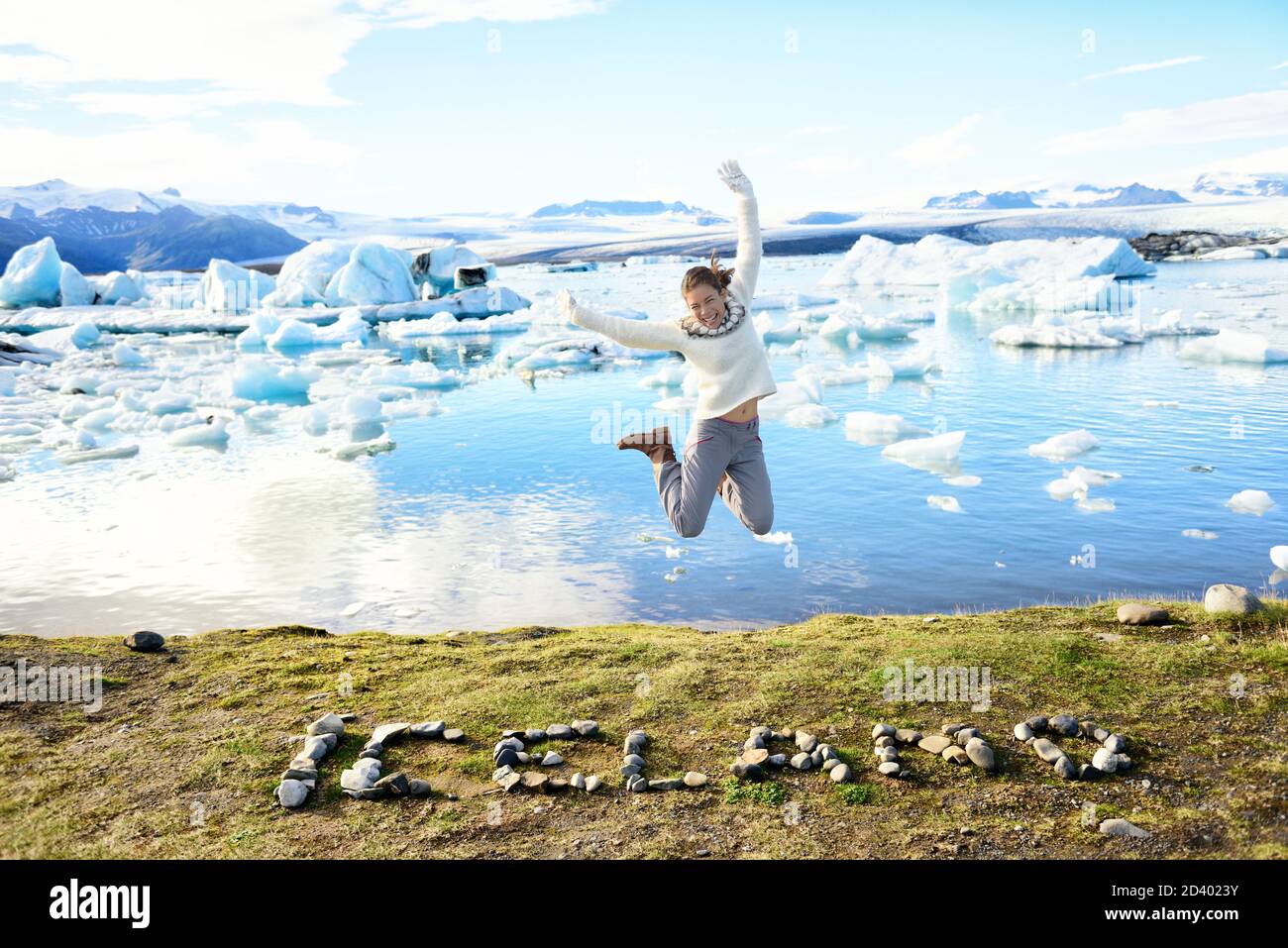 Iceland nature landscape Jokulsarlon glacial lagoon. ICELAND text written with rocks. Woman jumping having fun visiting tourist destination landmark Stock Photo