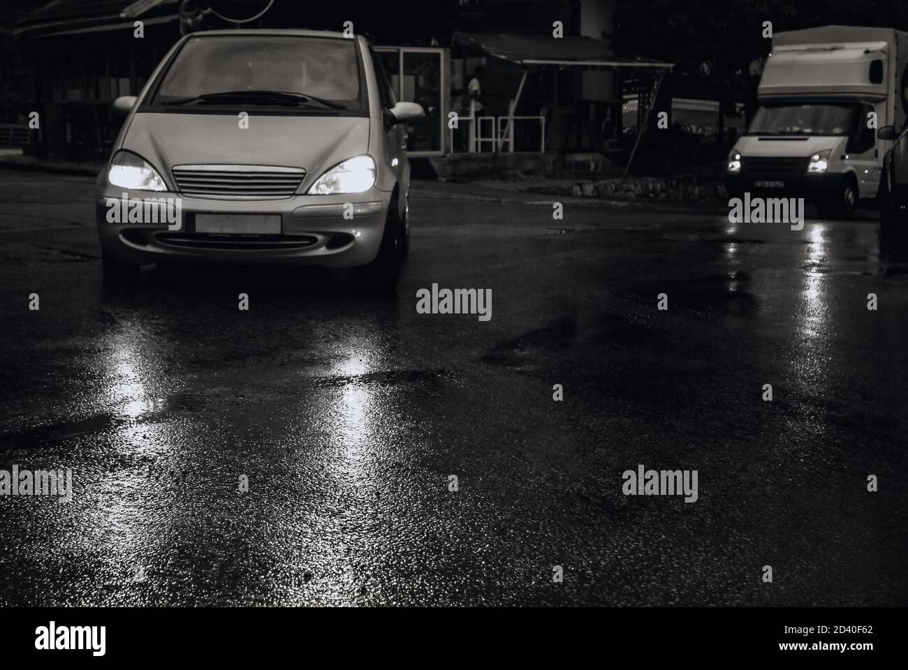 Cars with lights on crossing the street at night on wet road lights