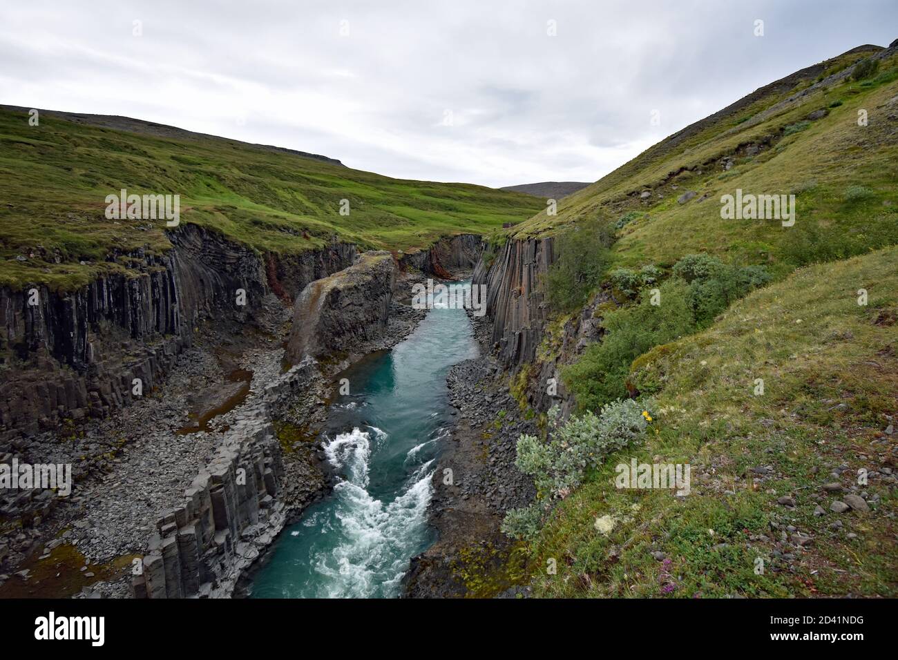 The blue, green Jokla River cuts through the Studlagil canyon and passes by the hexagonal basalt columns caused by lava flows in Northeast Iceland. Stock Photo
