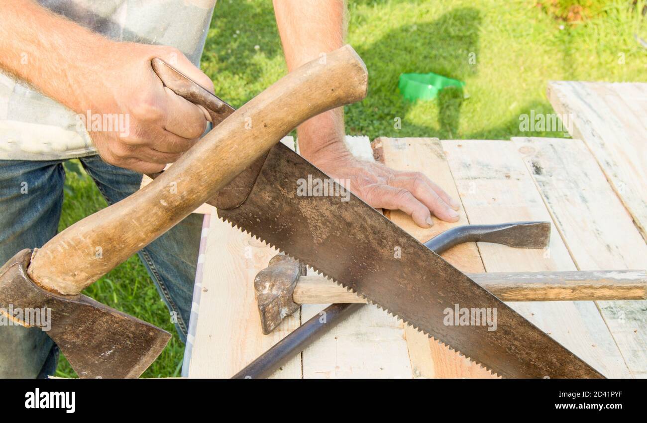 man uses a hacksaw, a hatchet, a claw hammer for construction work in