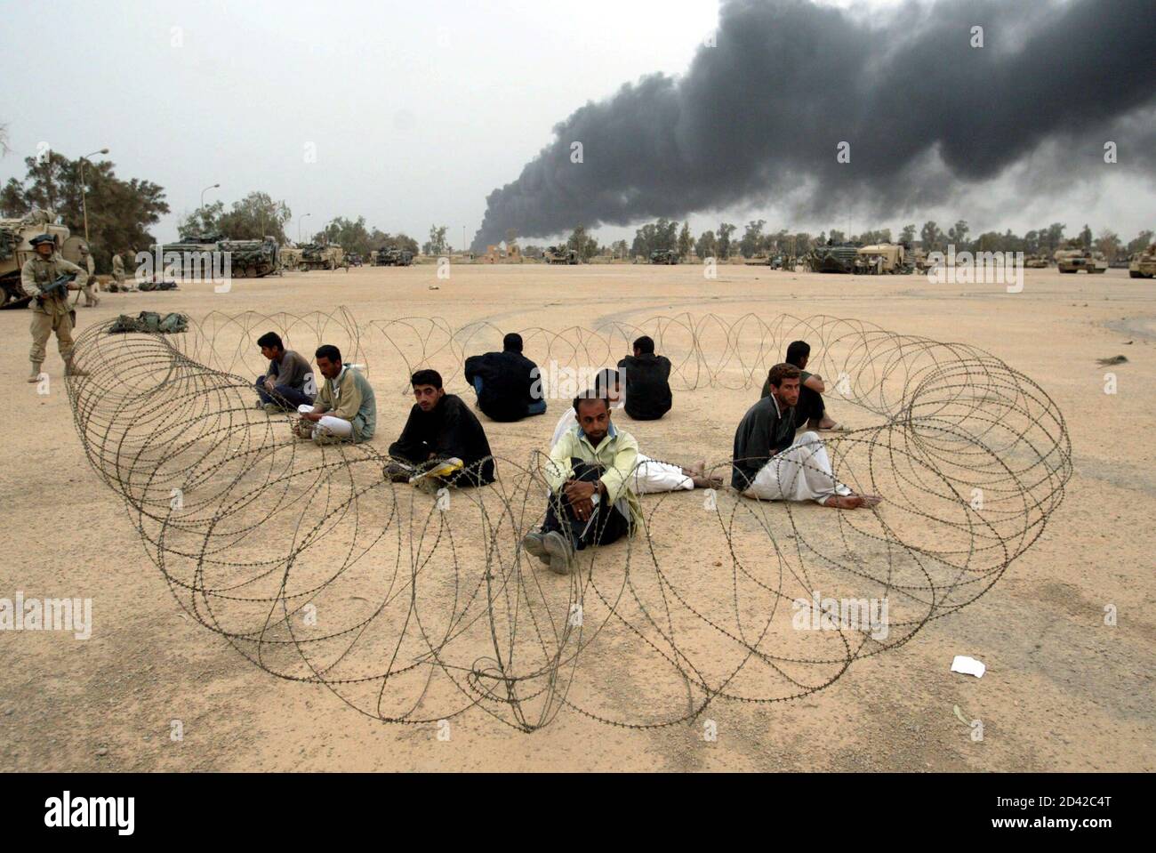 Members of the Iraqi Republican guard, dressed in civilian clothes, sit behind barbed wire at an abandoned Iraqi military base under the control of U.S. Marines in the suburbs of the Iraqi capital Baghdad on April 8, 2003.  U.S. Marines attacked a military airfield on the southeastern outskirts of Baghdad on Tuesday, as U.S. forces tried to tighten their noose around the Iraqi capital, a Reuters correspondent said. Military sources said the Marines would gradually push forward towards the city centre. Stock Photo