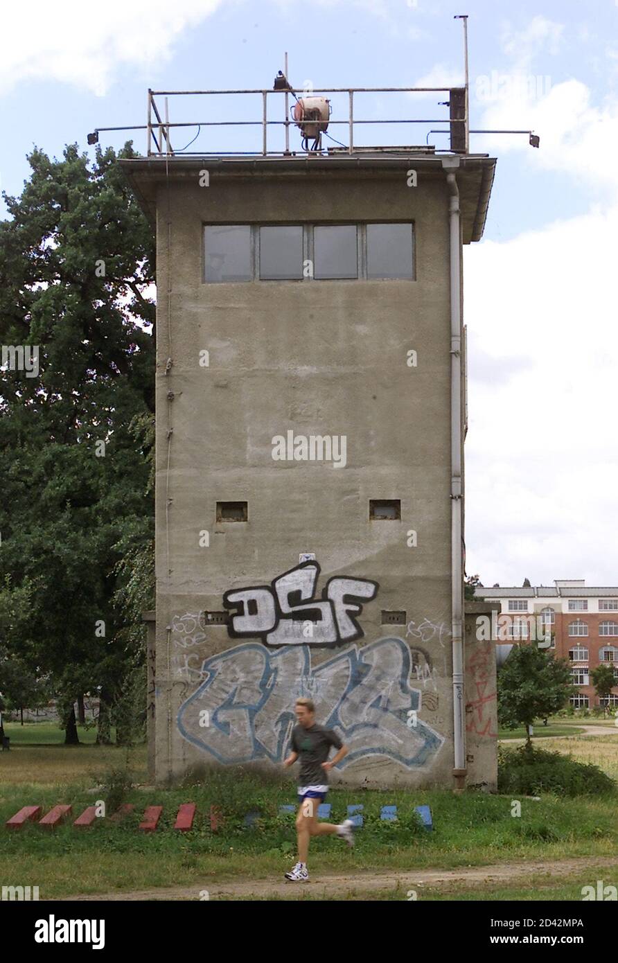 A man joggs in front of a watch tower at the Berlin Wall, the former East German frontier in Berlin-Treptow August 1, 2001. All that is left of the barrier built 40 years ago on August 13, 1961 by the Communist East German government is a grassy gap - a 30-metre (yard) wide 'death strip' surrounding the former capitalist enclave of West Berlin once used for East German border guard patrols - and a few chipped remnants.The converted death strip is nowadays an urban utopia, a traffic-free green zone of nature preserve in and around Germany's biggest city. Picture taken August 1, 2001.  AX Stock Photo