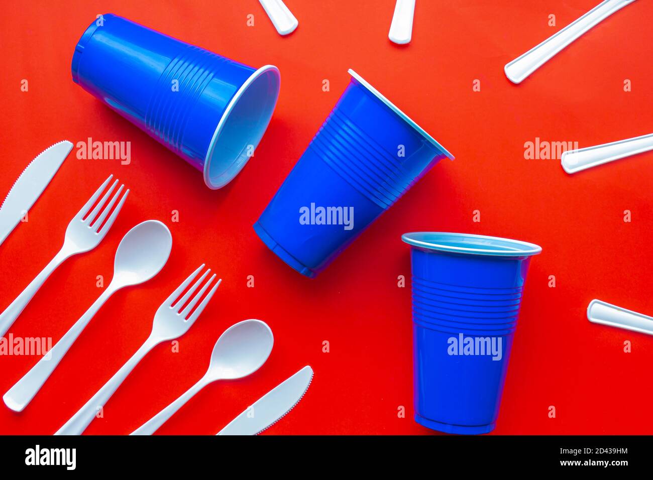 Single use white plastic cutlery and blue plastic glass on a red