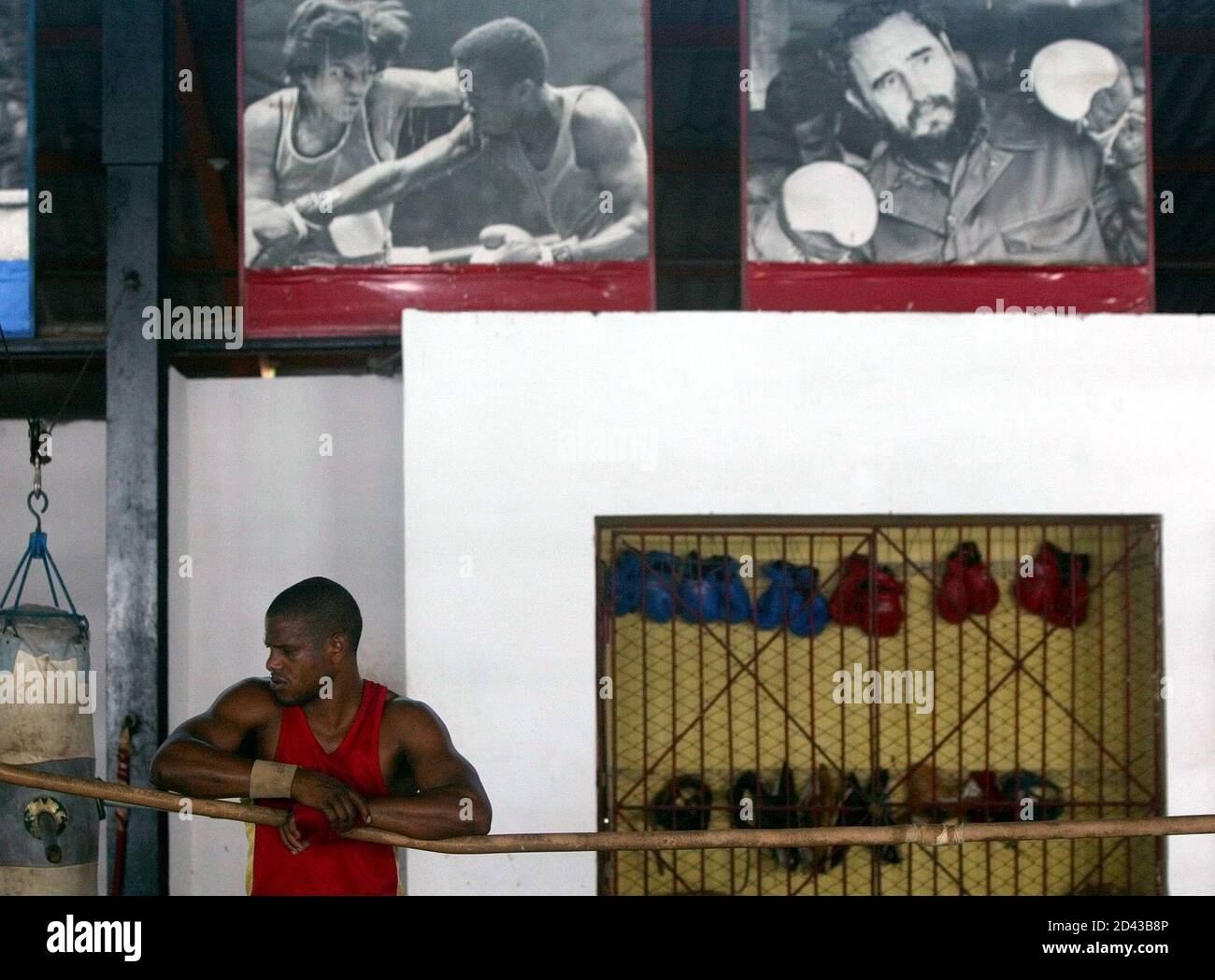 A Cuban boxer leans on a rope underneath pictures of Cuban three-time