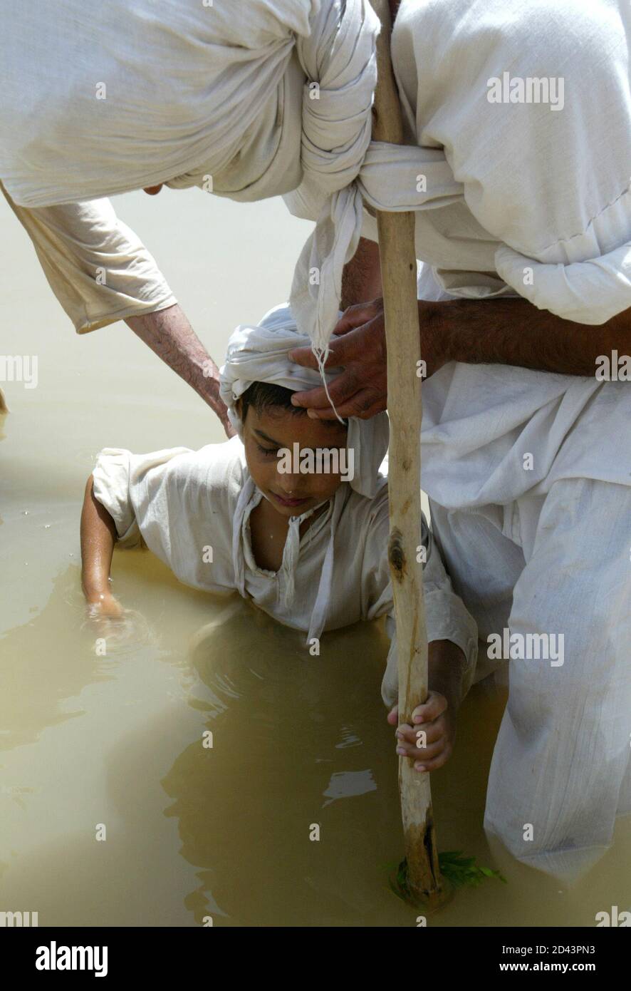 A young Iraqi Mandean boy is baptised in the Tigris river by a priest speaking the ancient Aramaic language during a wedding ceremony in Baghdad June 8, 2003. Iraqi devotees of an obscure religion who take John the Baptist as their central figure perform virginity tests on their brides and take a dip in the murky Tigris river every Sunday to purify the soul. Most of the world's 20,000 or so Mandeans live in southern Iraq and southwestern Iran. Stock Photo