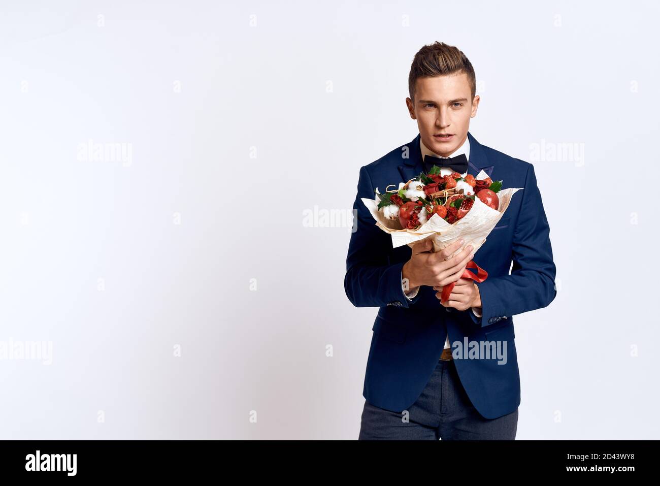 An elegant man in a classic suit with a bow tie holds a bouquet of ...