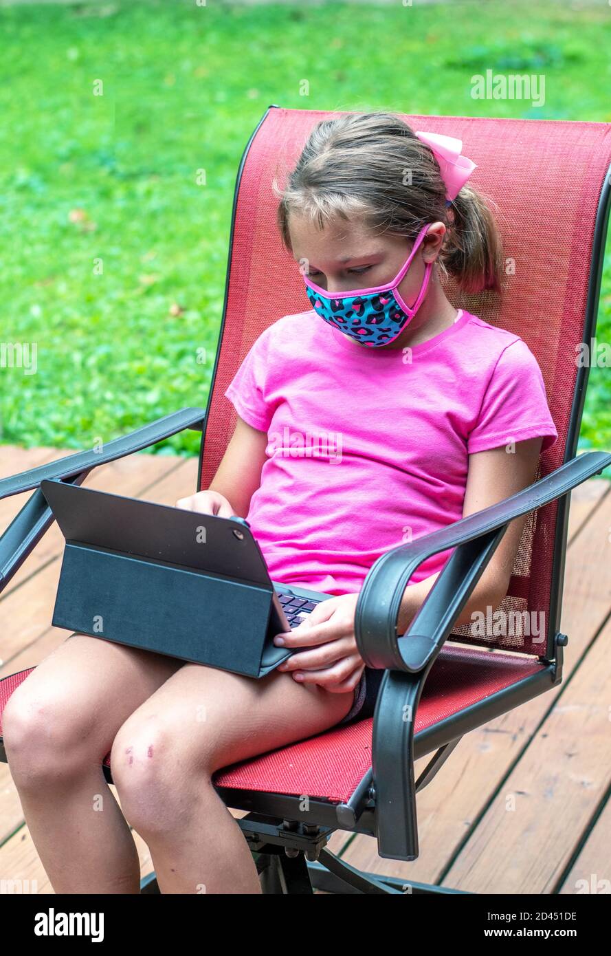 Young girl with tablet and mask sits on the deck to e-learn school classes from home Stock Photo