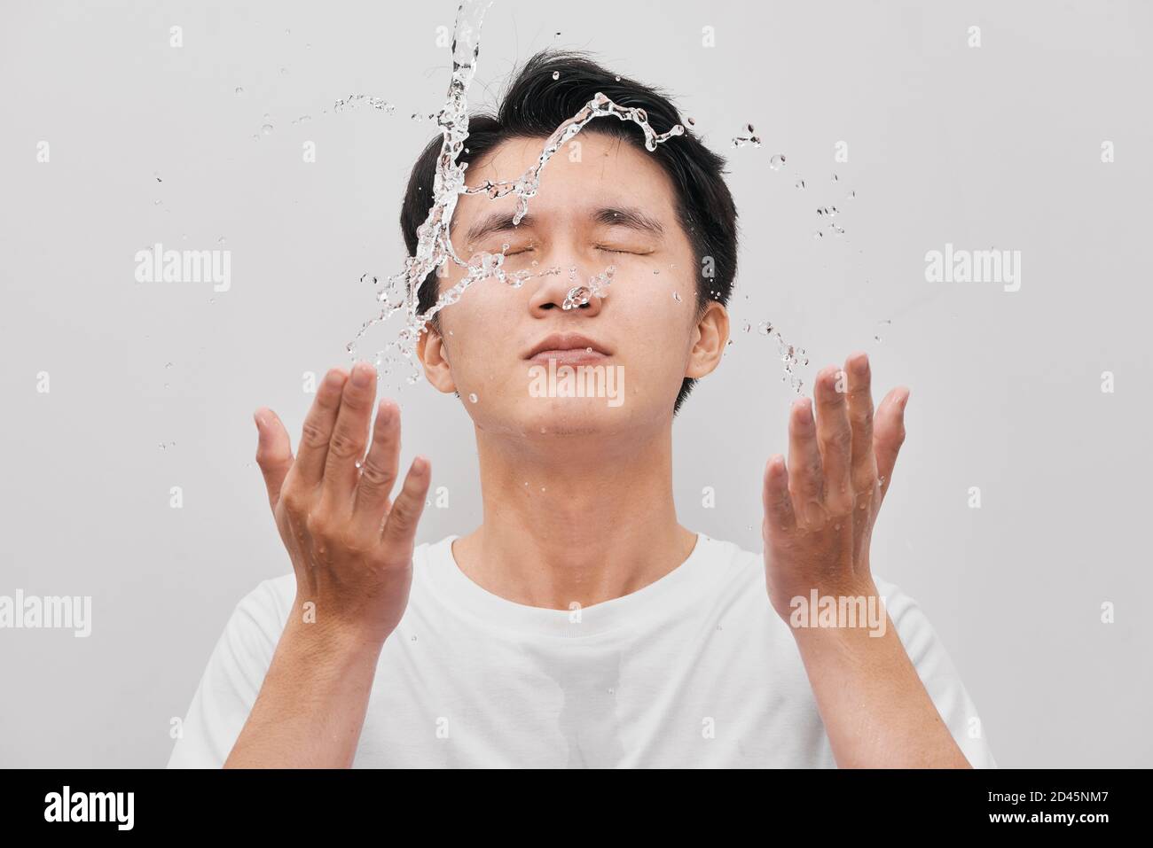 Young man spraying water on his face over gray background Stock Photo