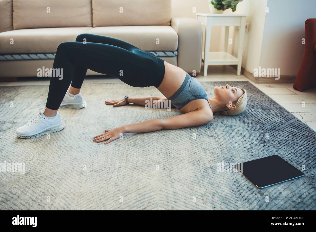 Caucasian woman in sportswear is planking during a digital fitness session at home using a tablet Stock Photo