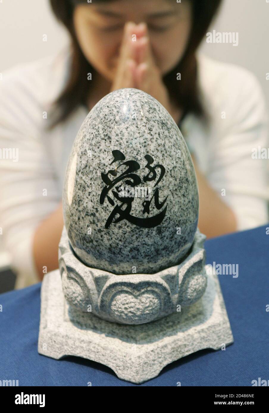 A Japanese Woman Folds Her Hands In Front Of A Small Oval Shaped Grave Where Ashes Of The Deceased Can Be Placed In Its Hallow Interior At An Exhibition In A Tokyo