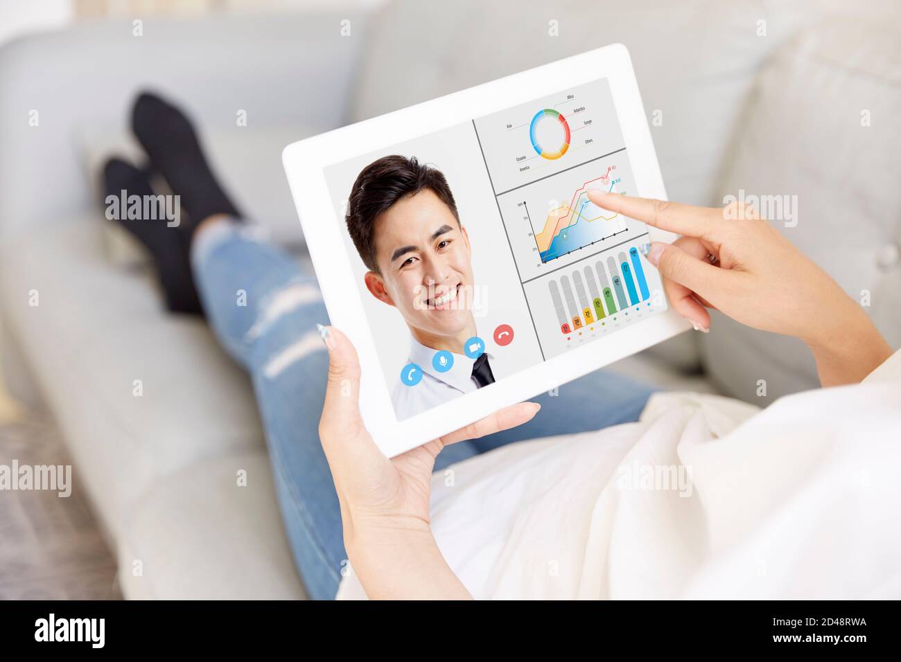 young asian businesswoman working from home sitting on couch dicussing business with male colleague via video call using digital tablet Stock Photo