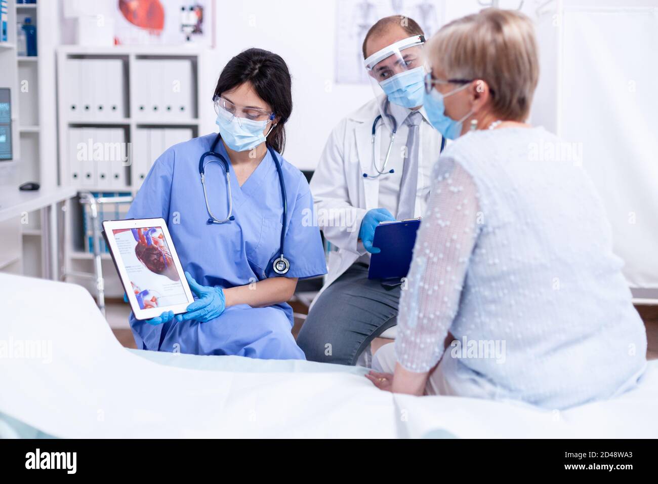 Cartdiologist telling senior woman what's wrong with her coronary artery during consulation in clinic examination room. Medical control for infections, disease and diagnosis. Stock Photo