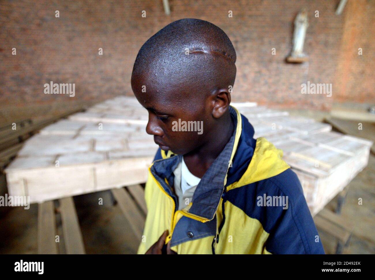 Rwandan genocide survivor Edmond Niyonsaba (16) shows his head scar made  with a machete April 4, 2004 in front of coffins with human remains ready  to be buried next week. Vowing never