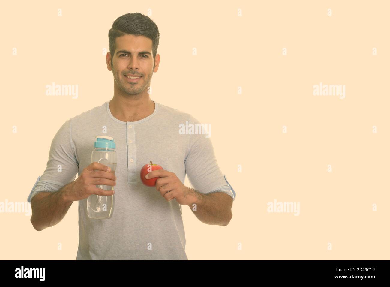 Young happy Persian man smiling and holding water bottle and red apple ...