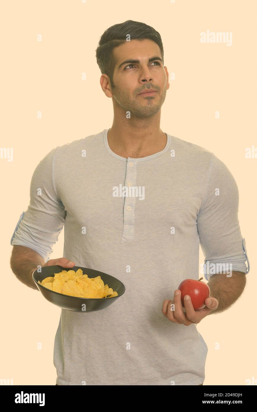 Young handsome Persian man holding bowl of potato chips and red apple ...