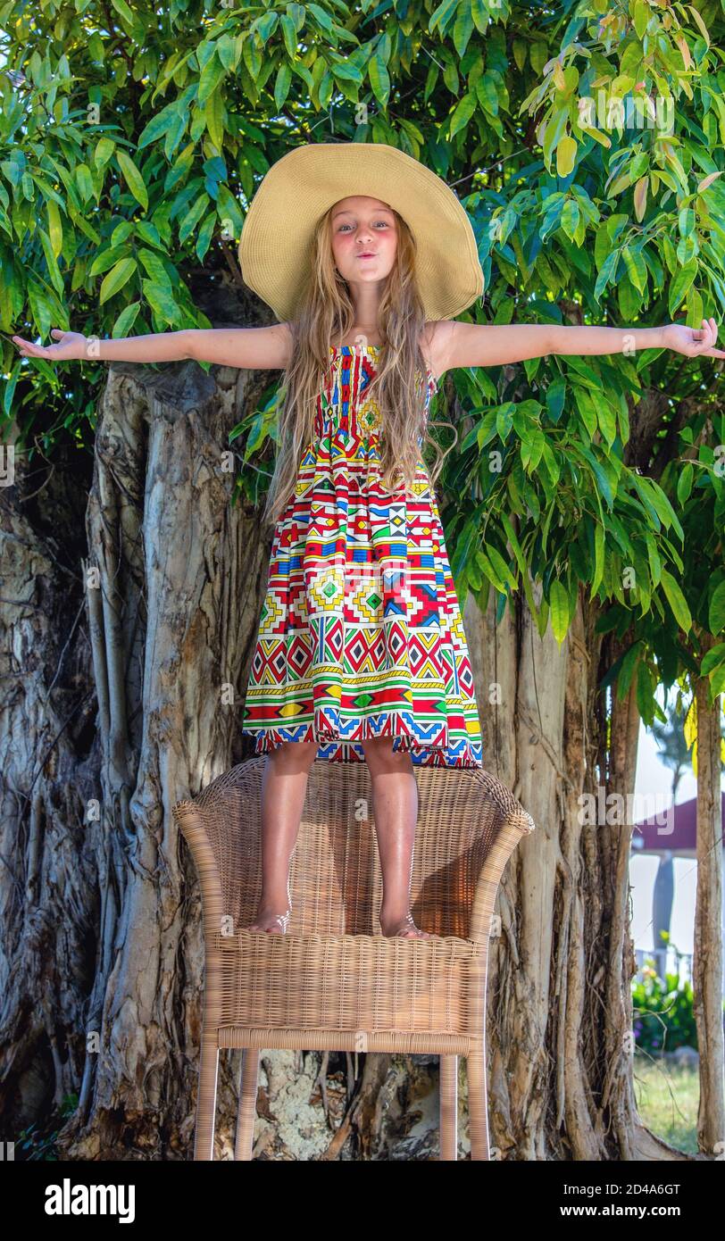 Little beautiful girl at tropical tree background. Portrait of cute child ready for tropical vacation. Stock Photo