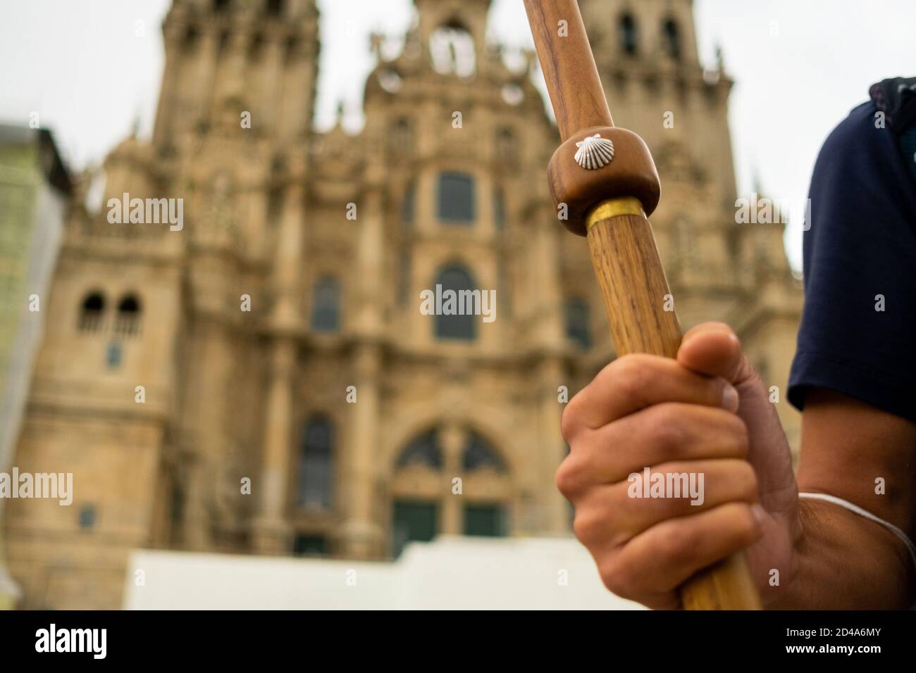 closeup of pilgrim hand holding walking stick with scallop shell, symbol of the camino de santiago pilgrimage, in front of the santiago cathedral Stock Photo