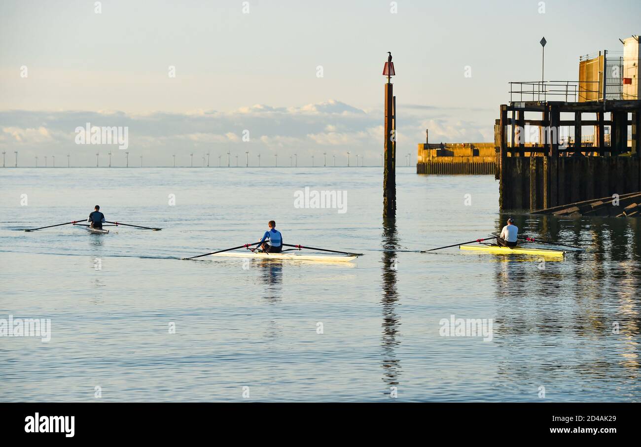 Brighton UK 9th October 2020 - A cormorant watches as rowers and scullers from Shoreham Rowing Club enjoy a beautiful calm sunny morning at Shoreham harbour near Brighton  . In the background the Rampion Wind Farm can be seen on the horizon : Credit Simon Dack / Alamy Live News Stock Photo