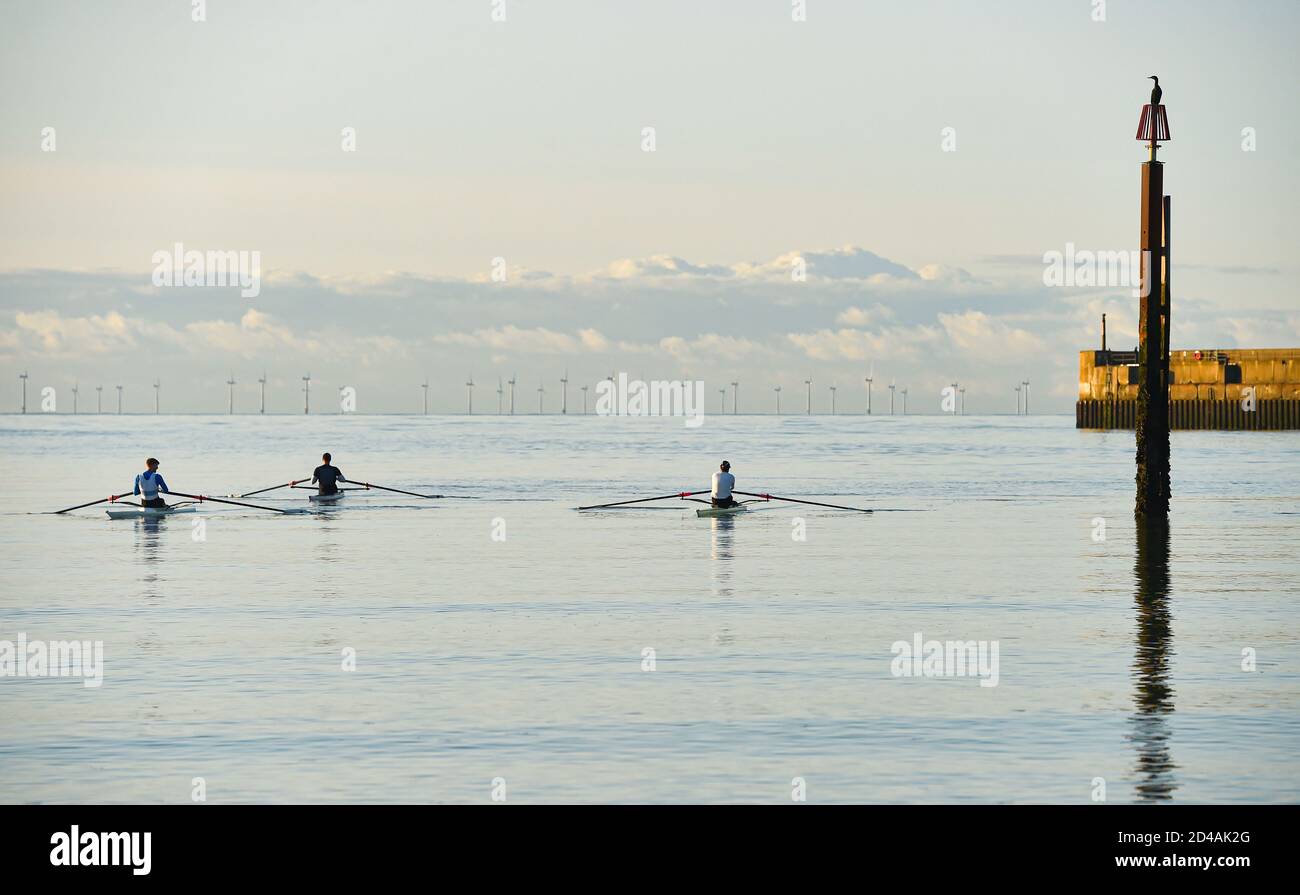 Brighton UK 9th October 2020 - A cormorant watches as rowers and scullers from Shoreham Rowing Club enjoy a beautiful calm sunny morning at Shoreham harbour near Brighton  . In the background the Rampion Wind Farm can be seen on the horizon : Credit Simon Dack / Alamy Live News Stock Photo
