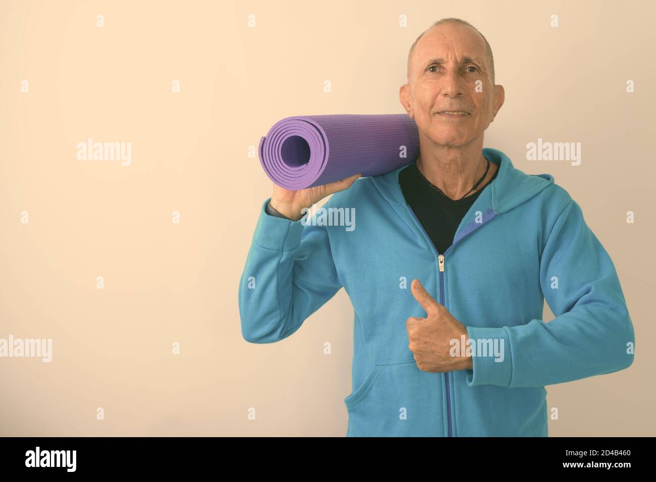 Studio shot of happy bald senior man holding yoga mat and giving thumb up ready for gym Stock Photo