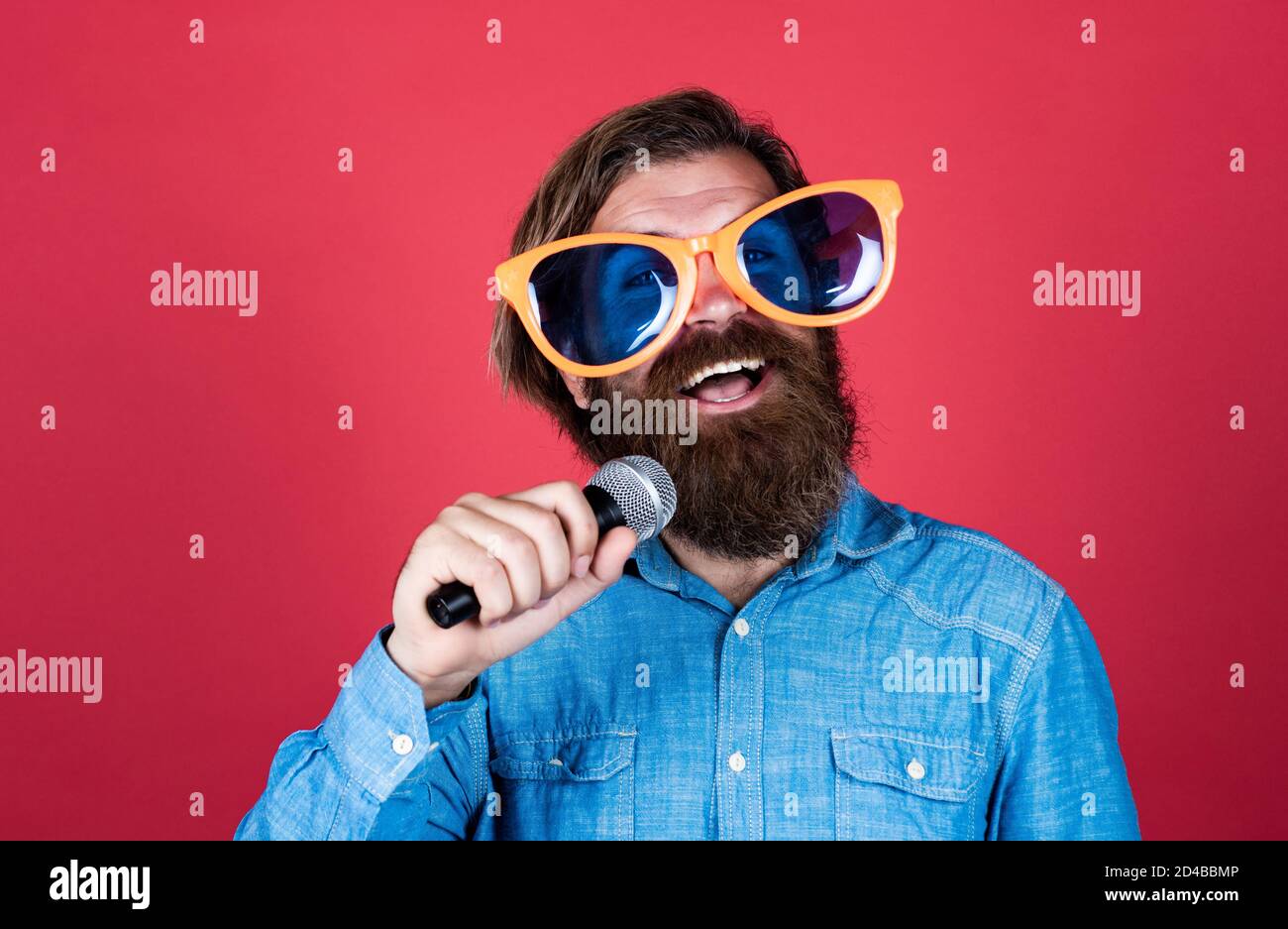party goer. hipster man with beard wearing glasses. music concept. have a happy holiday. have fun on party. male singer singing song in microphone. celebrate the anniversary. Stock Photo