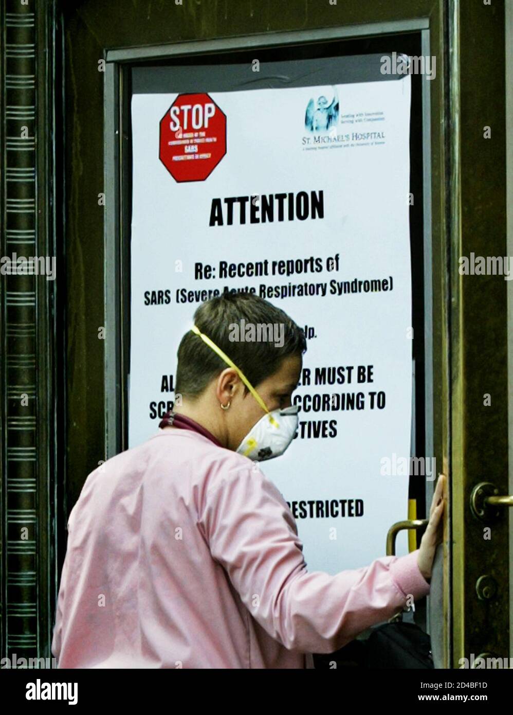 A health care worker, wearing a protective surgical mask to reduce the spread of Severe Acute Respiratory Syndrome (SARS), passes a sign warning of the reoccurrence of the deadly flue-like virus upon entering St. Michael's hospital in Toronto, May 26, 2003. Canadian health officials said on Monday they had detected about 20 more possible cases of SARS and warned of additional deaths as the World Health Organization put Toronto back on its list of SARS-infected areas, just 12 days after it was taken off. REUTERS/ Andrew Wallace  ANW/HB Stock Photo