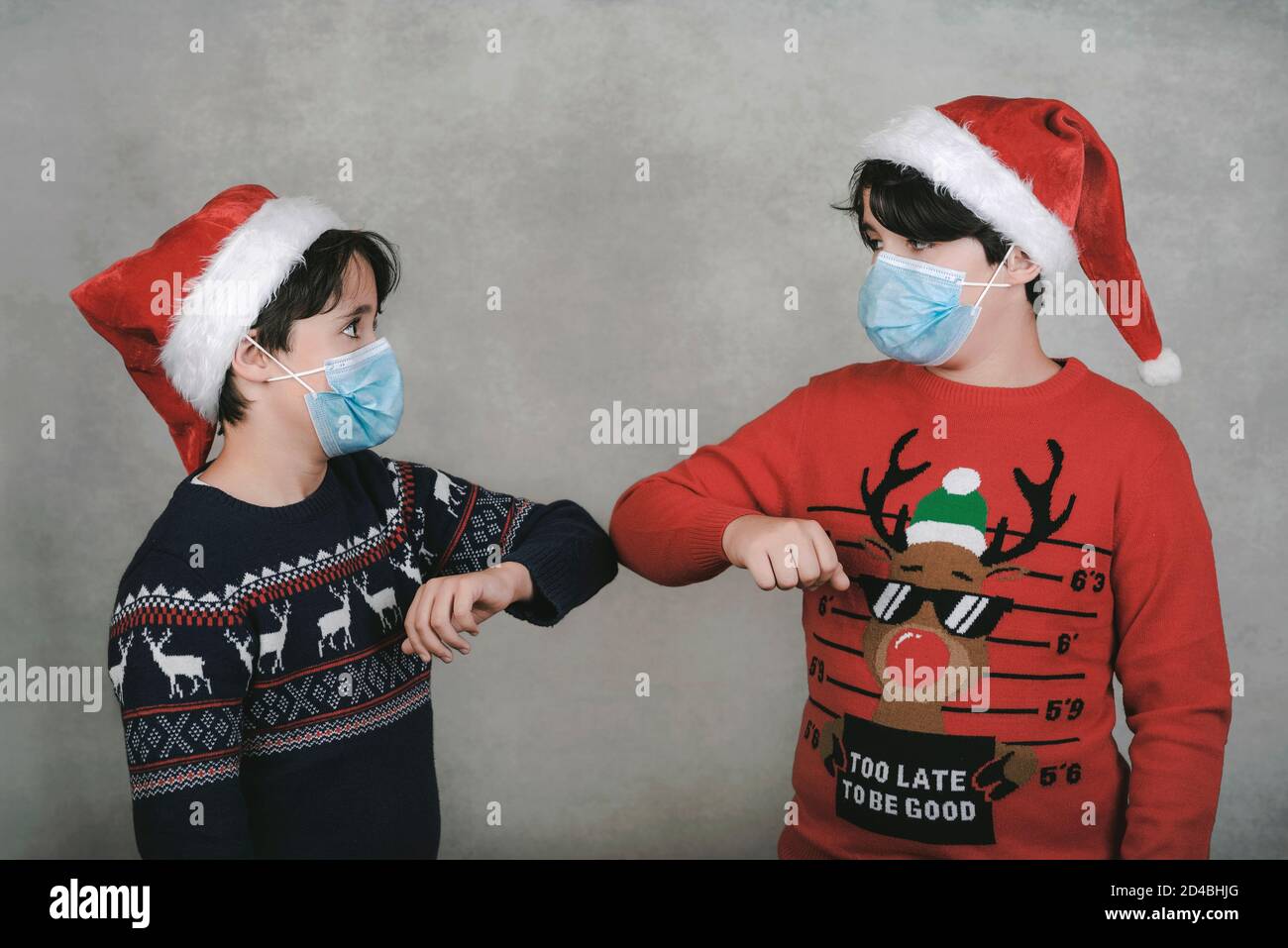 Merry Christmas,two kids with medical mask and Santa Claus hat bump elbows, social  distancing concept over gray background Stock Photo