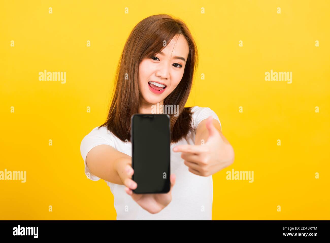 Asian happy portrait beautiful cute young woman smile standing wear t-shirt making finger pointing on smartphone blank screen looking to phone isolate Stock Photo