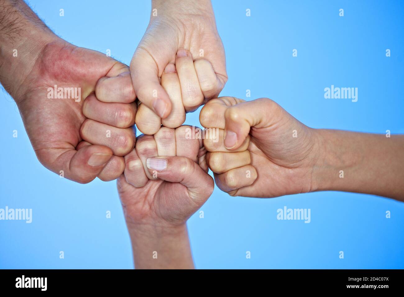 Four clenched fists meet against a blue sky Stock Photo