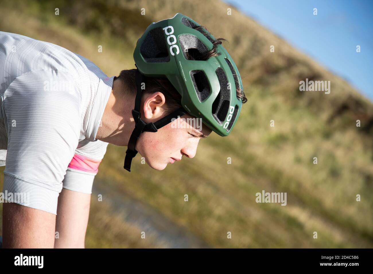 Head and shoulders close up in profile of a lone young cyclist wearing a bike helmet riding on the Yorkshire Moors with grassy background Stock Photo