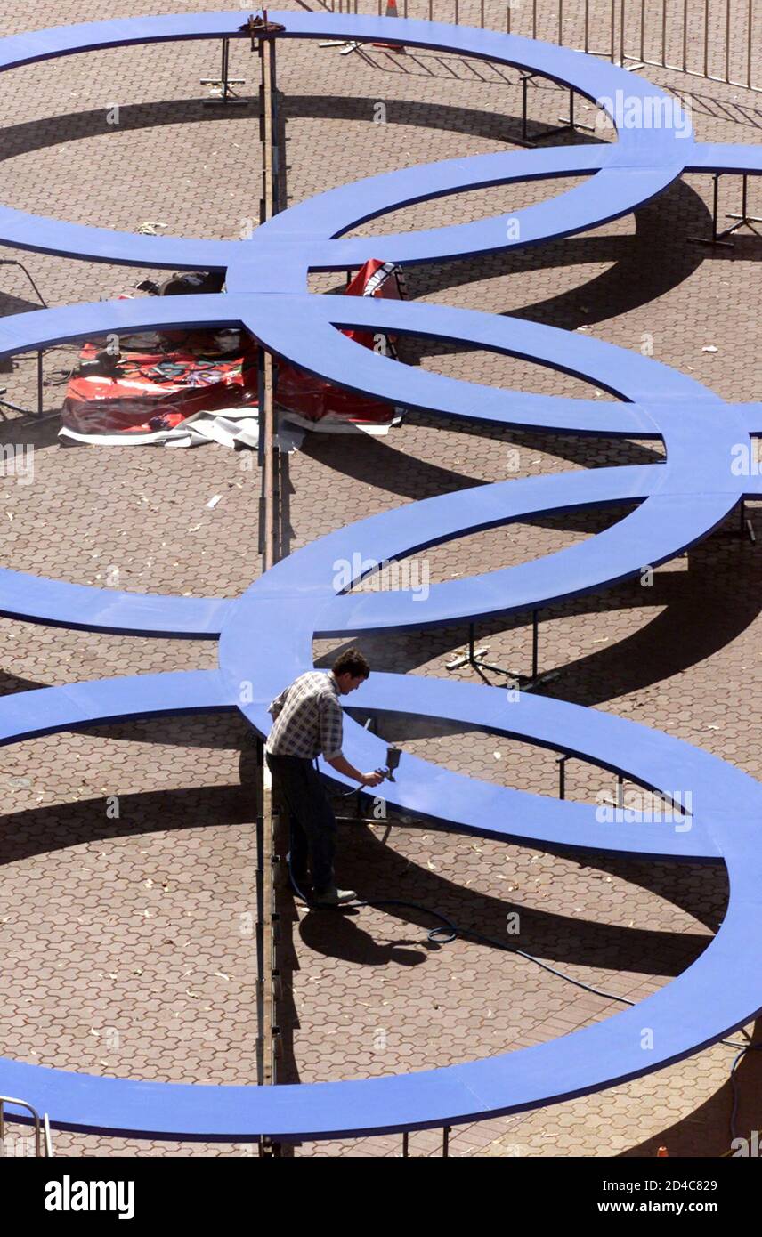A worker paints Olympic rings in front of the Sydney Olympic Stadium