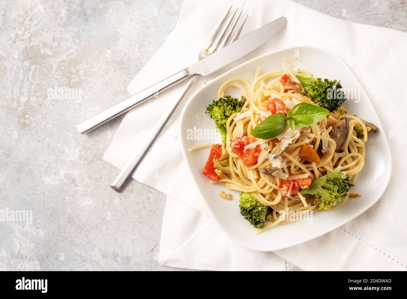 Spaghetti with tomatoes, broccoli, bell pepper, eggplant and herb garnish, healthy vegetarian pasta meal on a white plate and a light rustic backgroun Stock Photo