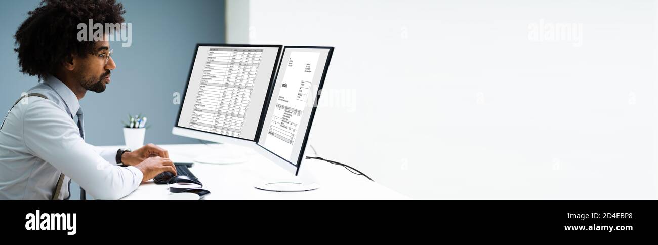 Looking At Invoice And Spreadsheet On Computer At Work Stock Photo