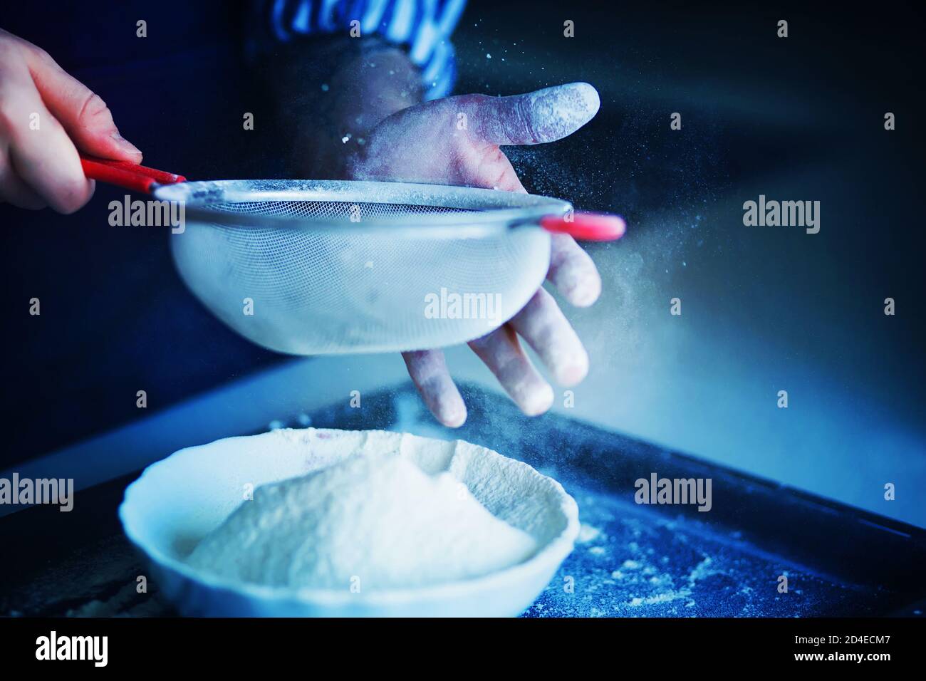 The cook holds a sieve of crumbly flour in one hand and helps sift it